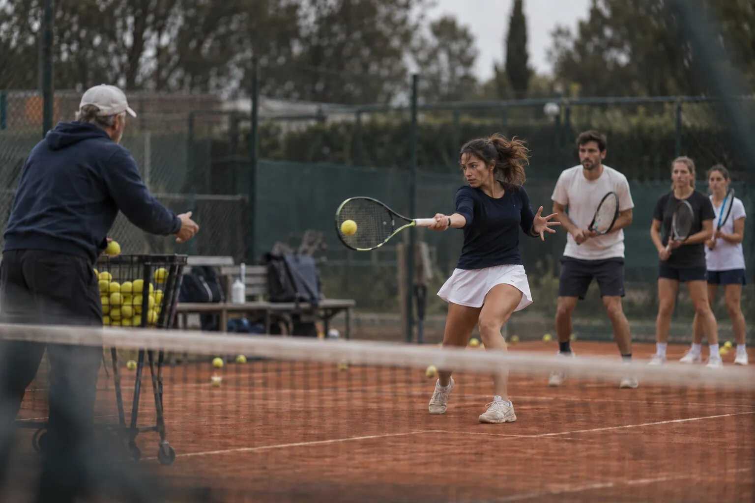 Un entraîneur de tennis envoie les balles, une joueuse frappe et la suivante attend son tour