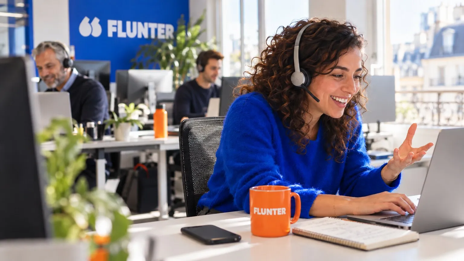 Commerciale souriante au casque en pleine conversation dans les bureaux Flunter